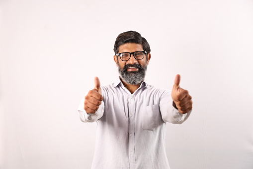 Conceptual background shoot of a happy Indian man with beard in spectacles showing thumbs up from both his hands.