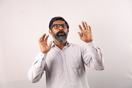 Conceptual background shoot of a happy Indian man with beard in spectacles giving coward expressions.