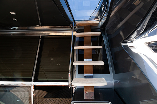 Access to the next floor of the yacht with a wooden staircase, railings and a closing hatch. Internal staircase on the yacht with handrails. Yacht interior with ladder.