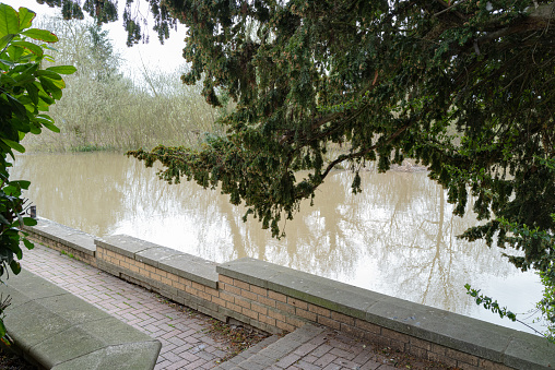 Local, English inland river seen about to burst its banks and flood the nearby walkway and town due to heavy rainfall.