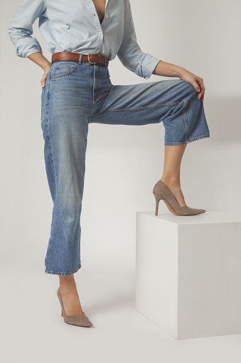 Studio shot of female model wearing wide leg jeans and suede high heels. Classic timeless fashion items.