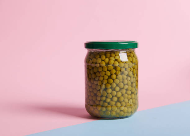 Glass can with green peas on a bicolor pink and blue background