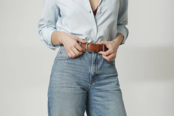 retrato da moda da mulher jovem no botão de algodão para baixo e jeans azuis ajustando seu cinto de couro marrom - belt leather fashion women - fotografias e filmes do acervo