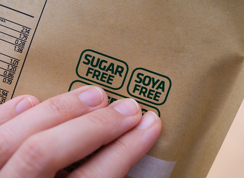 A woman holding a package with a Sugar Free and a Soya Free label on it. Close-up