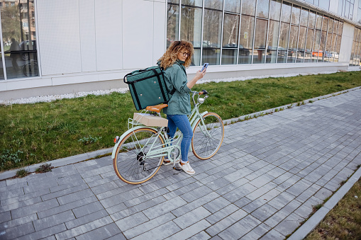 Woman bike courier using smartphone outdoors.