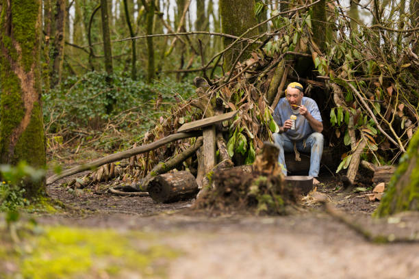 Homeless man in his 60s sitting by his pathetic bivouac eating a can of cold soup.