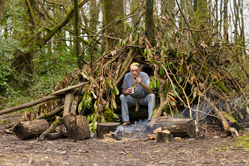 Homeless man in his 60s sitting by his pathetic fire and bivouac eating a can of cold soup.