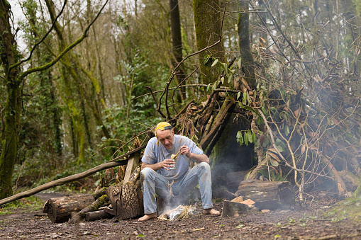 Homeless man in his 60s sitting in front of his woodland bivouac.