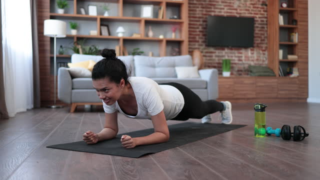 Sporty african woman in sport clothes training abs in plank position during regular workout at home