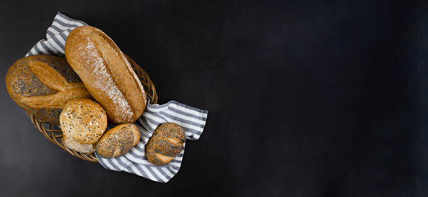 Fresh homemade baked goods in a basket on a black background. Copy space. Fresh bread.