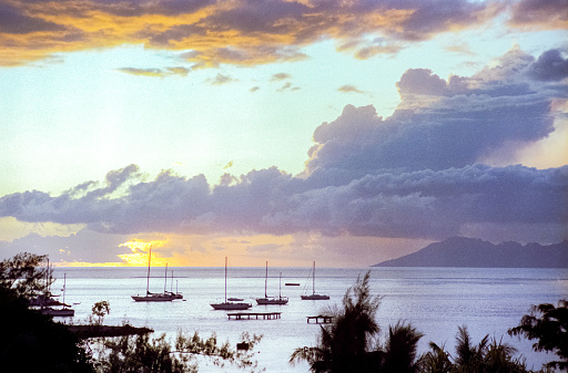 Film photograph of a vibrant Hawaiian volcanic orange sunset over the ocean horizon with sailboats in the water.