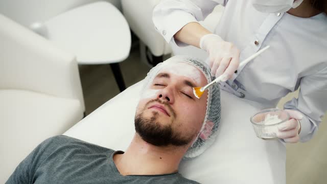 Unrecognizable beautician apply mask for face on man skin