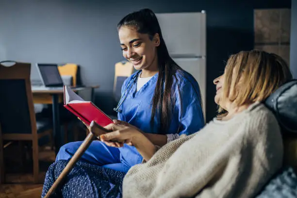 Photo of A nurse is reading a book to a senior patient