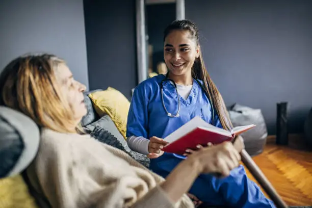 Photo of A nurse is reading a book to a senior patient