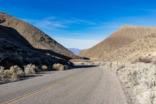 An empty paved road through scrub brush covered hills in the desert