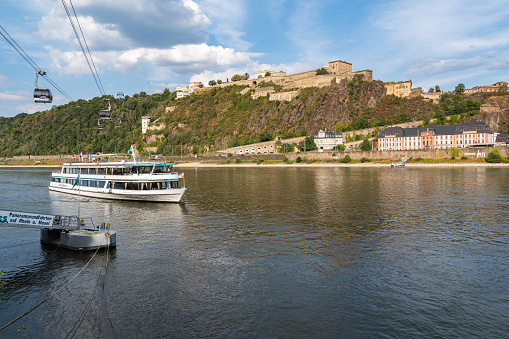 Ferry sailing in Rhine River in Koblenz with Ehrenbreitstein Fortress in the background, connected with the city by a cable car. Koblenz, Germany, Aug. 2022