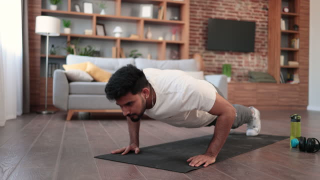 Attractive arabian man doing push up on yoga mat at living room.