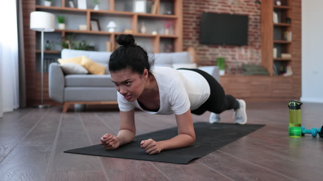 Sporty african woman in sport clothes training abs in plank position during regular workout at home