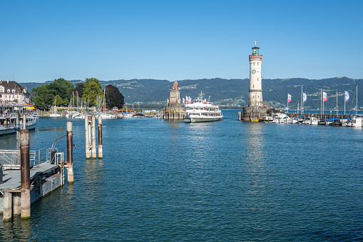 A ferry entering in Lindau port passing between the lighthouse and iconic Bavarian Lion sculpture. Lindau, Bavaria, Germany, Aug. 2022