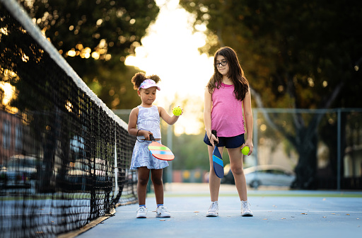 Two young Hispanic girls experience the excitement of their first day playing pickleball, eager to learn and have fun.
