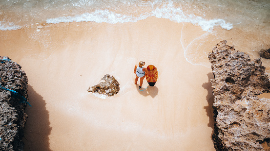 Aerial view of young woman with a surfboard standing on shore.