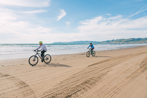Oceano, California, USA - March 27, 2023. Couple wearing cycling helmets riding bicycles on the beach, California central Coast