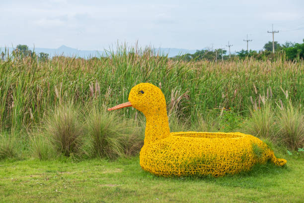 Big artificial yellow duckling or duck on green yard with long flower grass background at outdoor kid playground.
