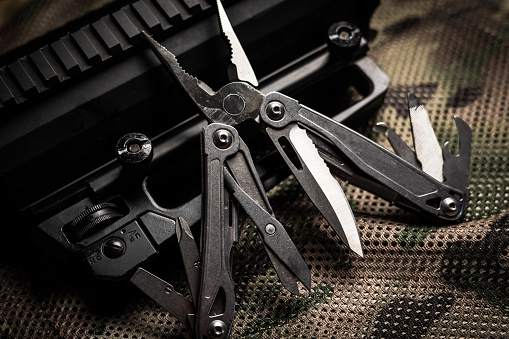 A steel multi-tool opened up to show the various tools displayed on a camouflage and tactical gear style background.