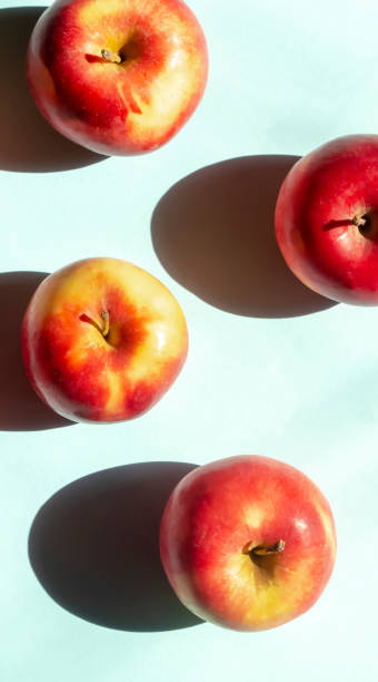 istock Bright sunlight falls on the apples creating a contrasting shadow. On a blue background lie red apples with yellow barrels. Vertical foto. 1478912662