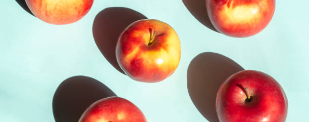 istock Bright sunlight falls on the apples creating a contrasting shadow. On a blue background lie red apples with yellow barrels. 1478912678
