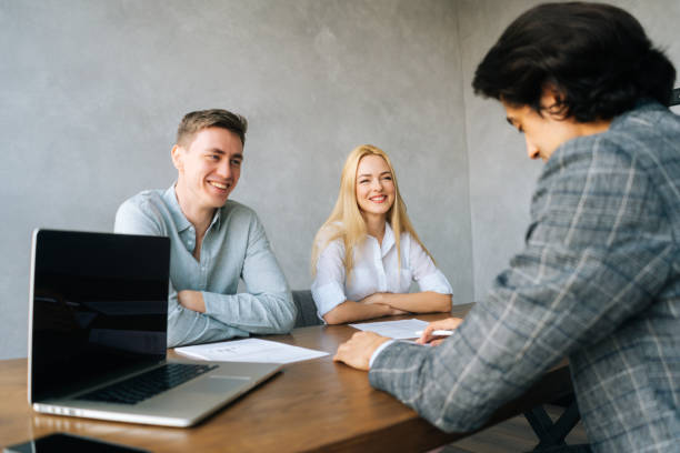 istock Back view of three cheerful young colleagues conducting business presentation while sitting at table with laptop and paper documents in boardroom. 1478913646