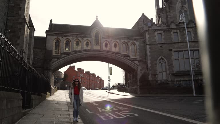 A stone bridge over a road, Christ Church Cathedral in Dublin-Ireland, Crowded city center, buildings and traffic, Dublin city center, woman pedestrian walking on the street, person walking on the sidewalk