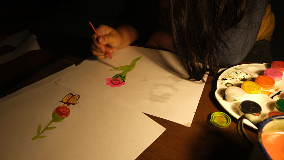 Kid hands making art by painting flowers in low light condition