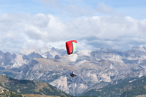 Red paragliding flying over the valley with the snowy mountain in the background and a nice sky with white clouds. Adventure activity in the Italian Alps from Col Rodella-Canazei-Italy in 09/22/2017.