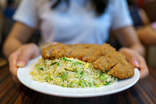 Cropped shot of an Asian woman holding a plate of pork cutlet fried rice in a restaurant, ready to eat.