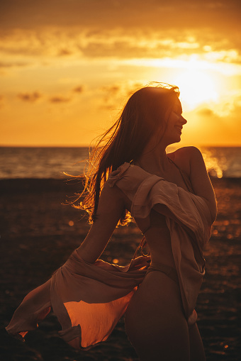 Dark silhouette of a man standing by the sea at golden sunset. Lonely teenager looking a setting sun.