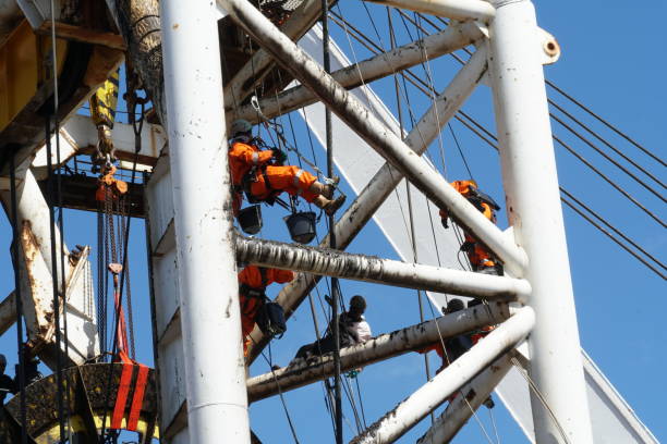 servicemen in orange overalls and helmets are hanging on the ropes and cleaning construction of vessel crane. - industrial ship shipping painting repairing imagens e fotografias de stock