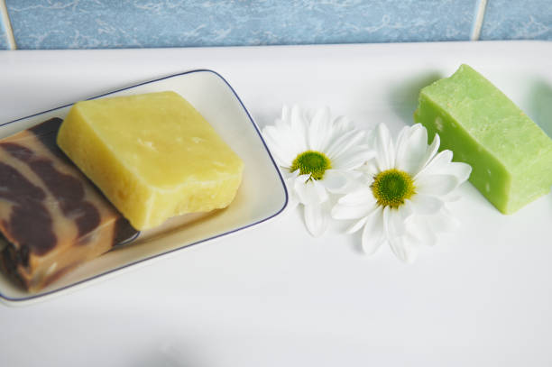 istock Selective focus on chamomile flowers and hand-made soap bars with natural herbal ingredients on white ceramic wash basin 1478985905
