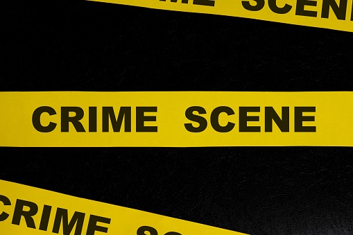 Crime scene yellow barricade tape warning and caution sign in dark black background.