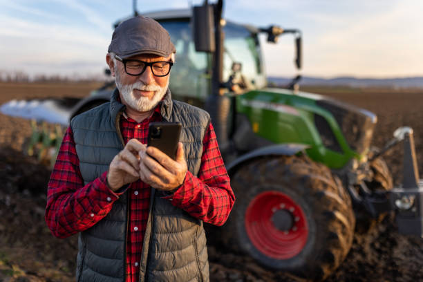 istock Senior farmer with mobile phone in field with tractor in background 1479011419
