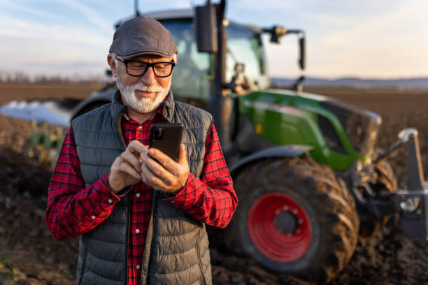 Senior farmer with mobile phone in field with tractor in background stock photo
