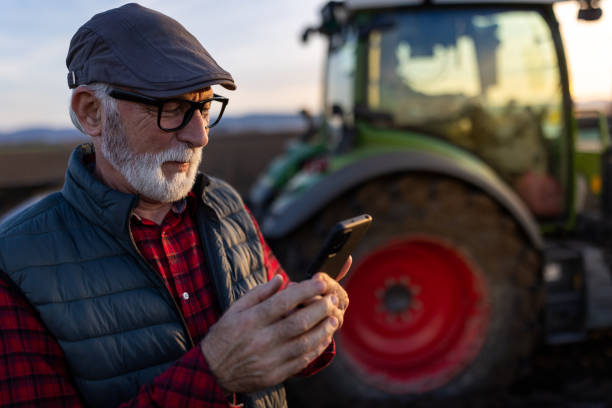 istock Senior farmer with mobile phone in field with tractor in background 1479011434