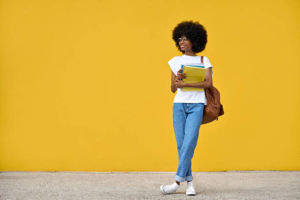 Fullbody portrait of a smart student looking aside on yellow background. stock photo