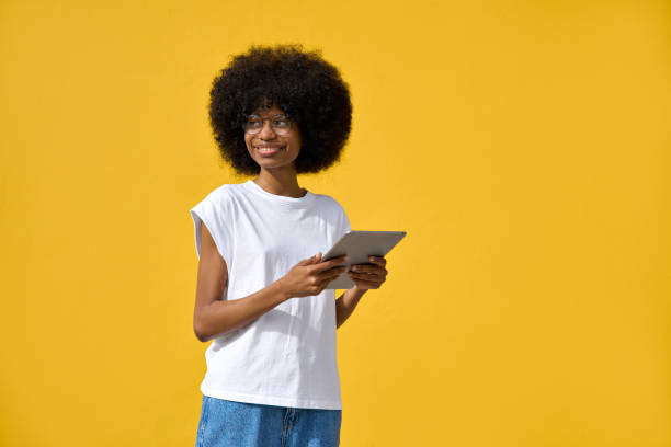 A woman using tablet in her hand and enjoy applications on yellow background stock photo