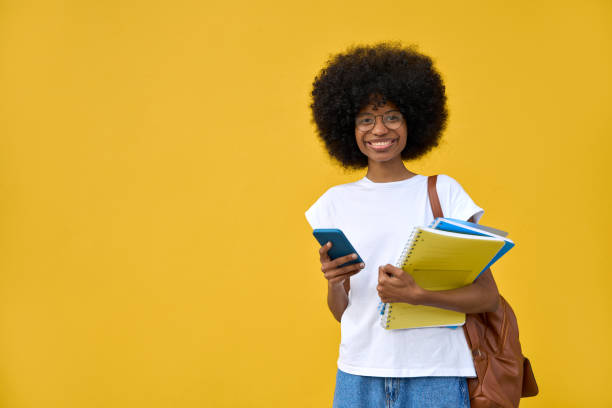 A student using phone in her hand and looking at her phone on yellow background stock photo
