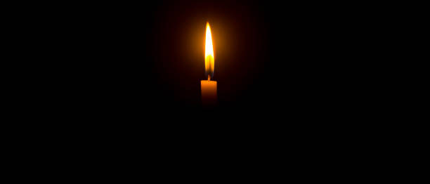 istock A single burning candle flame or light glowing on an orange candle on black or dark background on table in church for Christmas, funeral or memorial service with copy space 1479014903