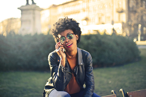 A young black female talking on her phone while sitting in the park