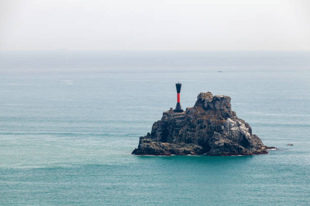 Isolated Danger Mark. Black beacon tower with red stripe is on a small rocky islet in the Sea of Japan near Busan city, South Korea