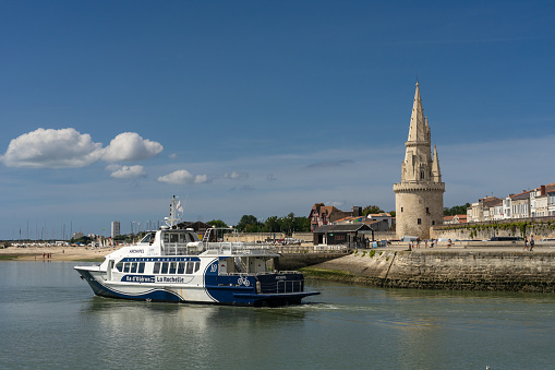 La Rochelle, France - August 26, 2022: Tourist boat leaving the old port of La Rochelle with the lantern tower in the background in a sunny day, France.