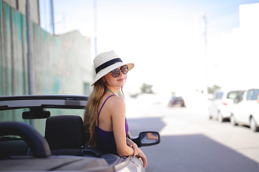 A young attractive lady with a white hat and sunglasses looking at the camera from the cabriolet